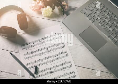 componi musica e formazione - foglio di carta con note musicali, laptop e cuffie sulla scrivania dell'artista Foto Stock