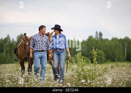 Coppia matura che portano i cavalli attraverso un prato Foto Stock