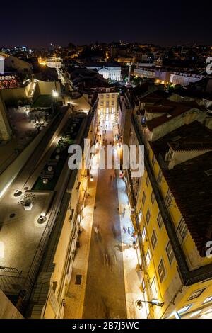 Vista degli edifici illuminati e delle persone sulla via Rua do Carmo verso Piazza Rossio nel quartiere Baixa a Lisbona, Portogallo, dall'alto di notte. Foto Stock
