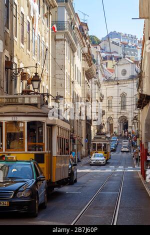 Due tram tradizionali nr. 28, auto e persone sulla strada Rua da Conceicao nel centro di Lisbona, Portogallo, in una giornata di sole. Foto Stock
