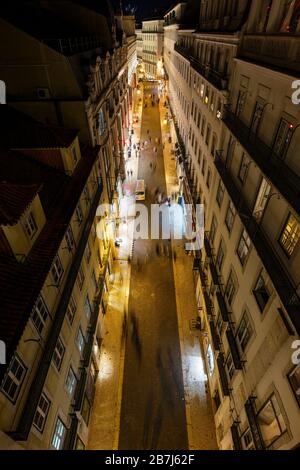 Vista degli edifici illuminati e delle persone sulla via Rua do Carmo nel quartiere Baixa a Lisbona, Portogallo, dall'alto di notte. Foto Stock