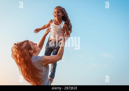 Giorno della madre. Donna che gioca divertendosi con la figlia nel parco primaverile. Madre che lancia la ragazza all'aperto e ridendo. Famiglia Foto Stock