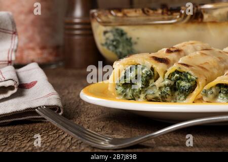 Un piatto giallo di cannelloni senza glutine con spinaci e formaggio casolare. Foto Stock