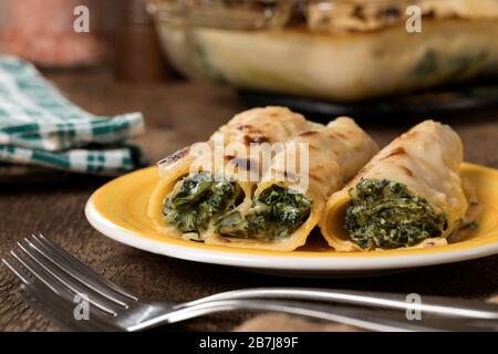 Un piatto giallo di cannelloni senza glutine con spinaci e formaggio casolare. Foto Stock