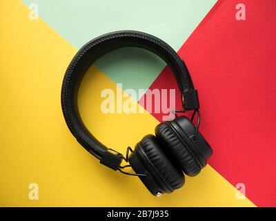 Cuffie wireless classiche nere su sfondo cartaceo colorato. Stile retrò. anni '80. Cultura pop. Vista dall'alto. Foto Stock