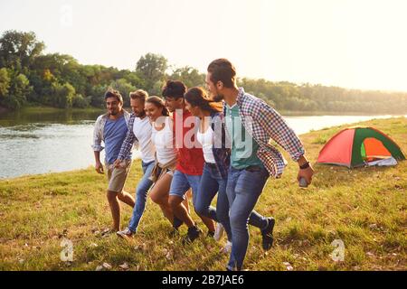 Gli amici hanno divertimento che corre lungo il lago su un picnic. Foto Stock