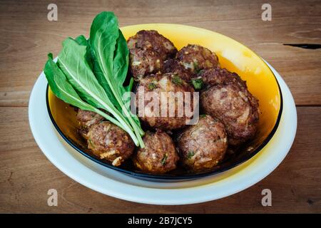 Polpette di manzo e verdure fresche crude a foglia di rucola, pronte a mangiare, in piatto sul rustico tavolo di legno Foto Stock