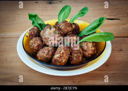 Polpette di manzo e verdure fresche crude a foglia di rucola, pronte a mangiare, in piatto sul rustico tavolo di legno Foto Stock