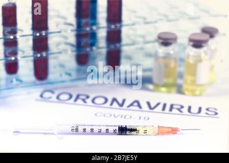 Siringa e flaconcini di vaccino con supporto per provette. Carta con la parola coronavirus e covid-19. Virus, vaccini e concetti di trattamento Foto Stock