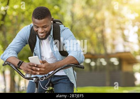 Ritratto all'aperto di giovane afro sorridente in bicicletta utilizzando lo smartphone Foto Stock