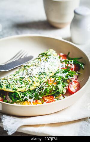 Frittata di spinaci verdi con formaggio, rucola e pomodori su un piatto bianco. Foto Stock