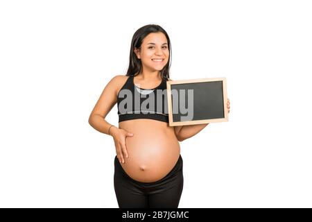 Primo piano della donna incinta che tiene e mostra qualcosa sulla lavagna. Gravidanza, maternità e promozione e concetto. Foto Stock