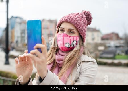 Donna che indossa la maschera corona facendo selfie con il telefono Foto Stock