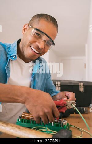 Ritratto del giovane latino che fissa problema di elettricità con cavi a casa nuova. Riparazione e ristrutturazione concetto casa. Foto Stock