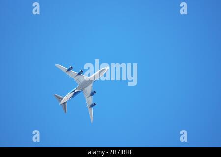 Aeroplano che vola nel cielo blu chiaro, vista dal basso. Aereo commerciale a quattro motori durante il decollo Foto Stock