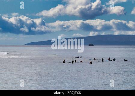 Surfers in attesa della prossima ondata nell'oceano a Lahaina su Maui con Lanai sullo sfondo. Foto Stock