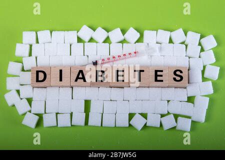 diabete di parola in blocchi di legno circondato da cubetti di zucchero su sfondo verde, siringa Foto Stock