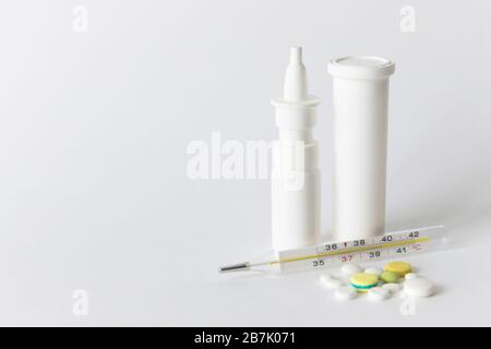 Primo piano della medicina spray nasale, flacone per pillola bianco, pillole colorate e termometro a mercurio medico, isolato su sfondo bianco con spazio per la copia. Influenza, Foto Stock