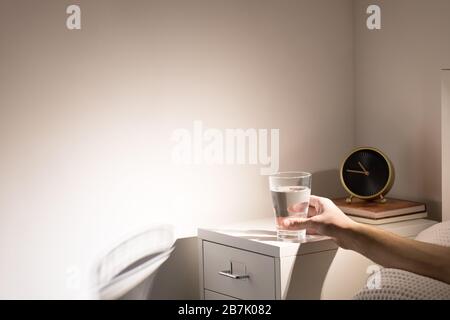 Buona abitudine - bere un bicchiere d'acqua prima di andare a dormire. Uomo a letto prendendo un bicchiere d'acqua dal comodino prima di andare a dormire, spazio copia. Foto Stock
