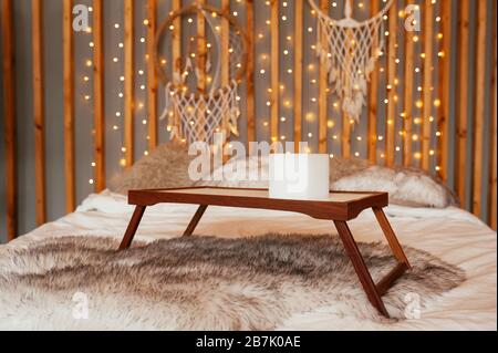 Tavolo in legno vuoto vassoio per la colazione a letto. Camera da letto boho, decorazioni in legno a parete con ghirlande, lampade e Dream Catchers. Foto Stock