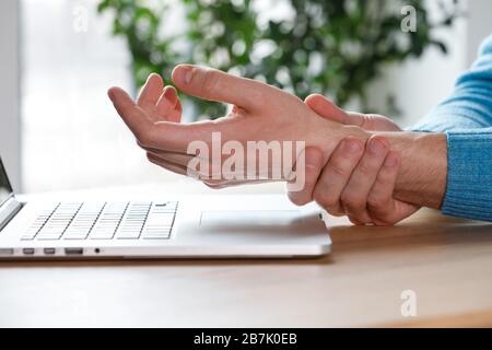 Primo piano delle braccia dell'uomo che trattengono il suo polso doloroso causato da un lavoro prolungato sul computer portatile. Sindrome del tunnel carpale, artrite, disea neurologica Foto Stock