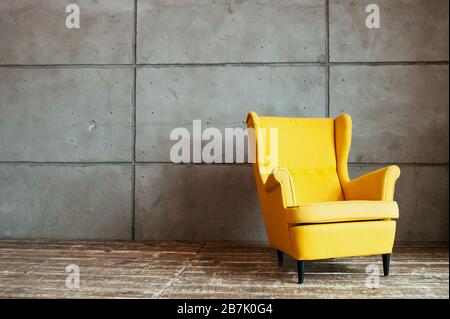 poltrona gialla fredda e robusta contro una parete grigia e irregolare di cemento e su un pavimento di legno scuro. Interni minimalistici in stile loft. Foto Stock