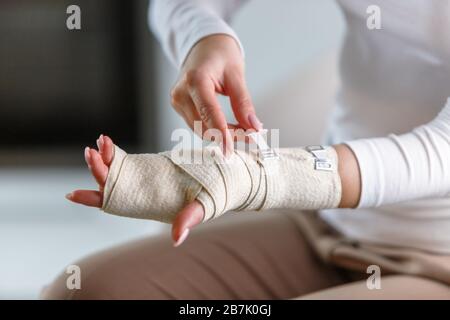 Primo piano della donna che avvolge il suo polso doloroso con bendaggio ortopedico elastico di supporto flessibile dopo sport o lesioni non riusciti. Tunnel carpale sy Foto Stock