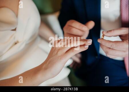 Lo sposo in una tuta blu mette un anello d'oro sulla mano della sposa in un abito bianco elegante. Mani del primo piano, senza facce. Foto Stock