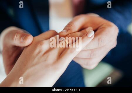 Lo sposo in una tuta blu mette un anello d'oro sulla mano della sposa in un abito bianco elegante. Mani del primo piano, senza facce. Foto Stock