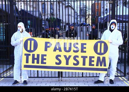 CORONAVIRUS COVID-19 2020. METTI IN PAUSA IL BANNER DEL SISTEMA TENUTO DA DUE UOMINI COPERTI DI INDUMENTI PROTETTIVI FUORI DOWNING STREET, WESTMINSTER, LONDRA, INGHILTERRA, REGNO UNITO. 16 MARZO 2020. Foto Stock