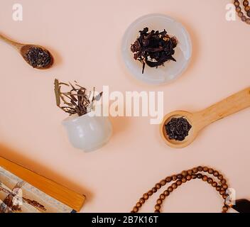 Immagine quadrata di una festa cinese del tè. Granuli secchi di diversi tipi di tè in una tazza di pietra bianca, in cucchiai di legno su delicato fondo rosa. Retro Foto Stock