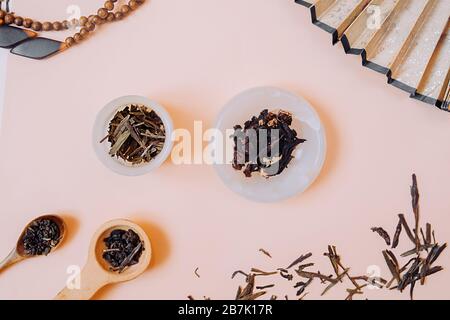 Festa cinese del tè. Granuli secchi di diversi tipi di tè in una tazza di pietra bianca, in cucchiai di legno su un delicato fondo rosa. Lo sfondo è decorato Foto Stock