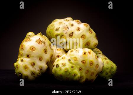 Molta frutta di Noni o formaggio raggruppata con varie sfumature di colore contrastate su uno sfondo scuro Foto Stock