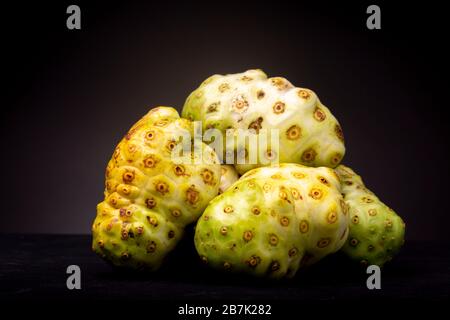 Noni o formaggio frutta raggruppata con varie tonalità di colore contrastato su uno sfondo scuro Foto Stock