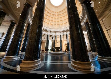 WASHINGTON, DC, Stati Uniti: La grande rotunda della National Gallery of Art di Washington, DC, mostra l'architettura neoclassica con la sua imponente cupola, il lucernario e le colonne corinzie. Una fontana centrale aggiunge un elemento dinamico allo spazio circolare, che funge da ingresso principale e punto focale del museo. Il design della rotonda, caratterizzato da un layout simmetrico e proporzioni classiche, esemplifica la visione dell'architetto John Russell Pope. Foto Stock