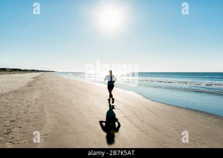 SOUTH CAROLINA, Stati Uniti: Una donna fa jogging lungo la costa di una spiaggia del South Carolina mentre il sole sorge sull'Oceano Atlantico, gettando un bagliore dorato sulla distesa sabbiosa e sulle dolci onde. Foto Stock