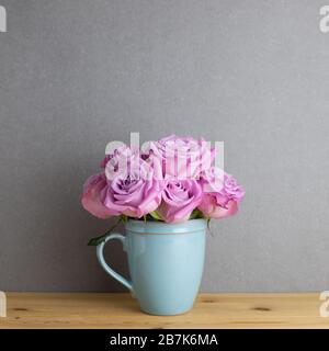 Fiori di rosa viola in tazza di ceramica su tavolo di legno con sfondo grigio. Disposizione floreale primavera, spazio copia Foto Stock
