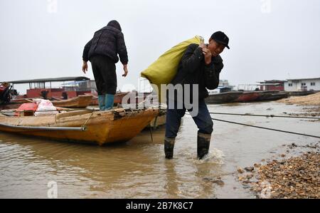 La gente sposta i bagagli da una barca da pesca vicino al lago Dongting nella città di Yueyang, nella provincia di Hunan della Cina centrale, il 30 dicembre 2019. Divieto di pesca di 10 anni t Foto Stock