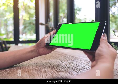 Immagine mockup delle mani che tengono un tablet PC nero con schermo vuoto sul tavolo in legno vintage Foto Stock