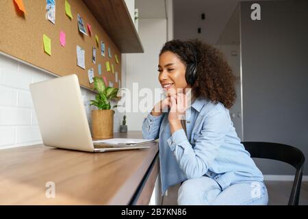 Giovane ragazza afro-americana sorridente indossare cuffie video chiamata sul laptop. Foto Stock