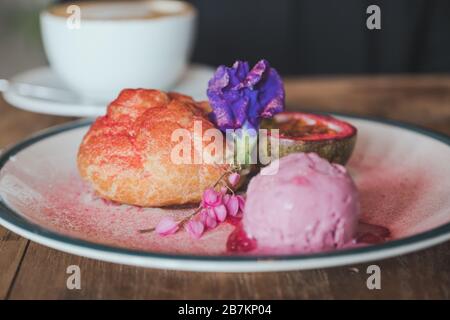 Immagine di primo piano di un piatto di Choux crema, rosato gelato e frutto della passione con bella decorazione e tazza di caffè in background Foto Stock