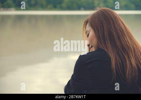 Immagine di primo piano di una donna asiatica seduta da sola vicino al fiume Foto Stock