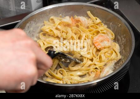 primo piano chef maschio frigge grandi gamberi re e pasta in olio d'oliva in una padella di metallo. Il processo di preparazione della pasta ai gamberi Foto Stock