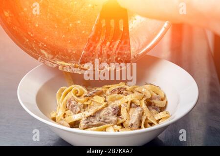 Lo chef Сlose-up maschile mescola grandi gamberi e pasta con salsa di crema da una padella a un piatto. Il processo di preparazione della pasta ai gamberi Foto Stock