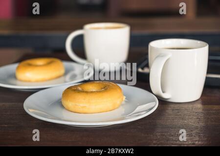 Due ciambelle in una piastra bianca con tazze da caffè su un tavolo di legno Foto Stock