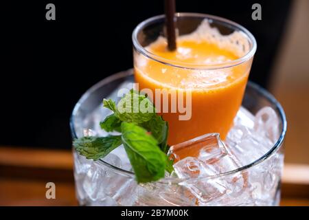 Un bicchiere di succo misto di arancia e carota in un vaso di ghiaccio con foglie di menta Foto Stock