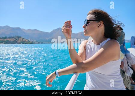 Bella donna matura ama il viaggio estivo in mare, femmina sul lato di una piccola barca da diporto. Mar Mediterraneo, Baia di Mirabello, isole greche all'orizzonte. Clea Foto Stock