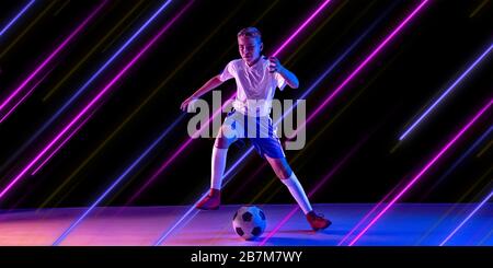 Sport creativo e linee al neon su sfondo scuro, volantino, proposta. Calcio maschile, allenatore di calcio in azione e in movimento. Concetto di hobby, stile di vita sano, gioventù, azione, movimento, stile moderno. Foto Stock