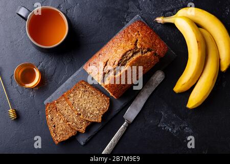 Banana, pane di cocco, torta con una tazza di tè su tavola di ardesia. Sfondo in pietra scura. Spazio di copia. Vista dall'alto. Foto Stock