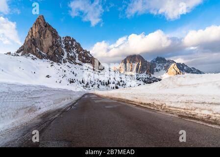 Deserta strada di montagna dominata da torreggianti vette rocciose coperte di neve in una limpida giornata invernale Foto Stock